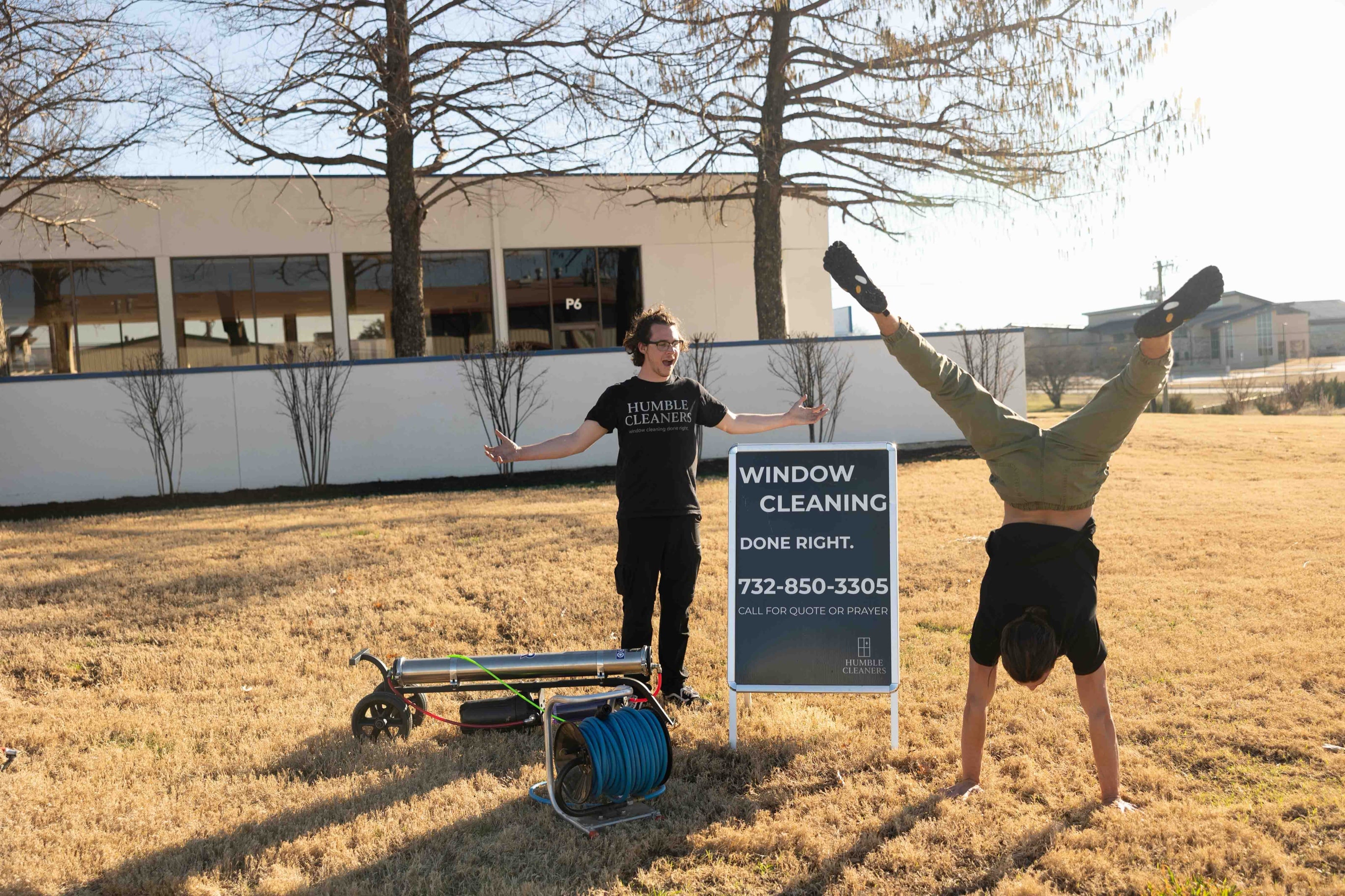 Two crew members celebrating beside the yard sign, one mid-handstand